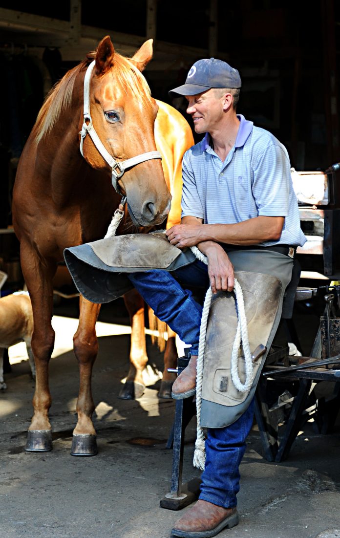Farrier Jordan Garrick sits atop and anvil stand as he visits with his 25-year-old personal horse Stanley out of his San Juan Bautista workshop. Garrick has been shoeing horses for 16 years, three of them out of this workshop.
