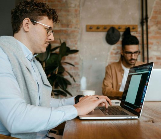 Two men type on laptops